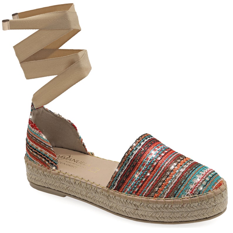 May include: Espadrille sandal with a woven upper in shades of red, orange, and teal, with a beige ankle wrap. The sole is made of woven jute. The sandal has a small wedge heel.