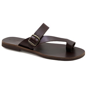 May include: Brown leather sandals with a buckle strap and a toe loop. The sandals have a flat sole.