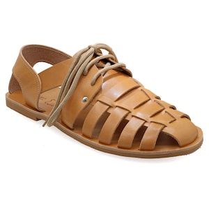May include: Tan leather sandal with a woven design on the top and a lace-up closure. The sandal has a flat sole and an open heel. The overall design is a classic, casual style, suitable for warm weather.