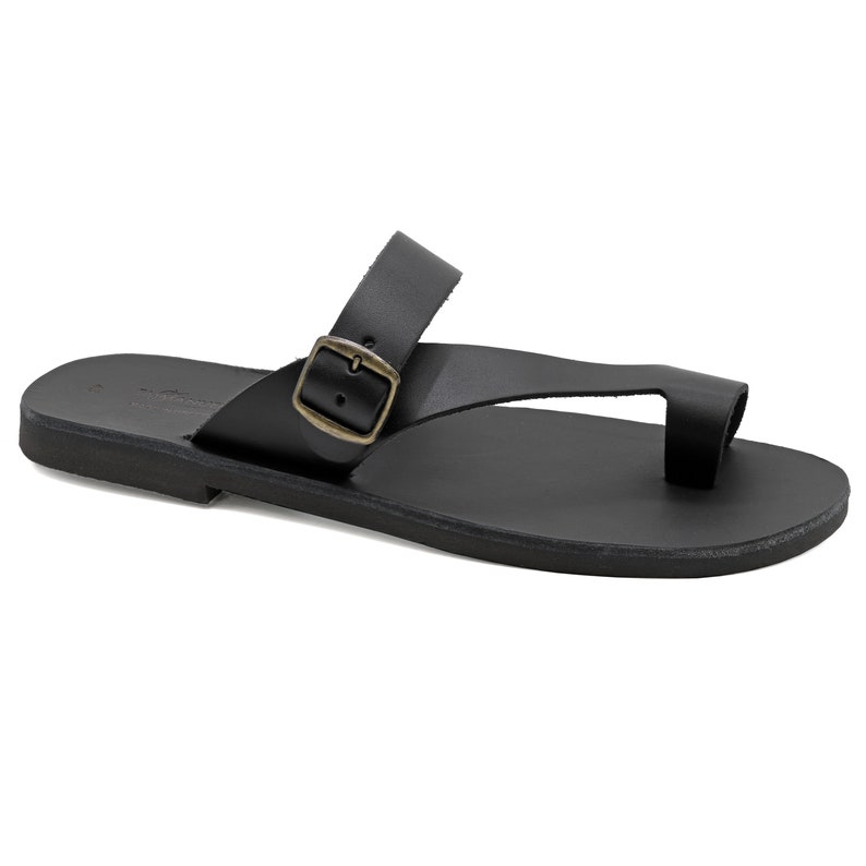 May include: Black leather sandals with a buckle strap and a toe loop. The sandals have a flat sole.