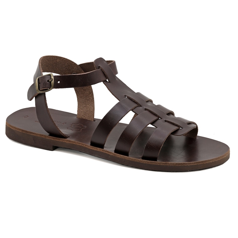 May include: A brown leather sandal with a woven design across the foot and an ankle strap with a buckle. The sandal has a flat sole and is designed for warm weather wear.