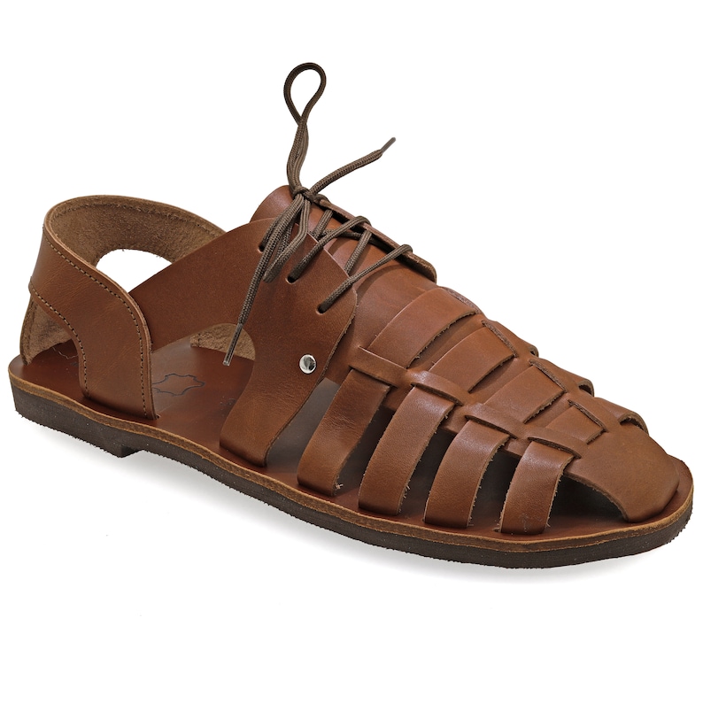 May include: Brown leather sandal with a woven design across the top. The sandal features a lace-up closure and a flat sole. The open-toe design and overall construction suggest a casual, comfortable style. The sandal is made of genuine leather.