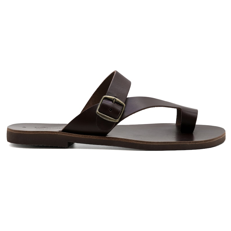 May include: Brown leather sandals with a buckle strap and a toe loop. The sandals have a flat sole.