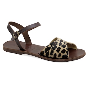 May include: Brown leather sandal with a leopard print accent. The sandal features a thin ankle strap with a buckle closure and a flat sole. The leopard print is black and brown.