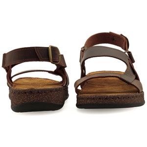 May include: A pair of brown leather sandals with a buckle closure. The sandals have a cork footbed and a brown rubber outsole.