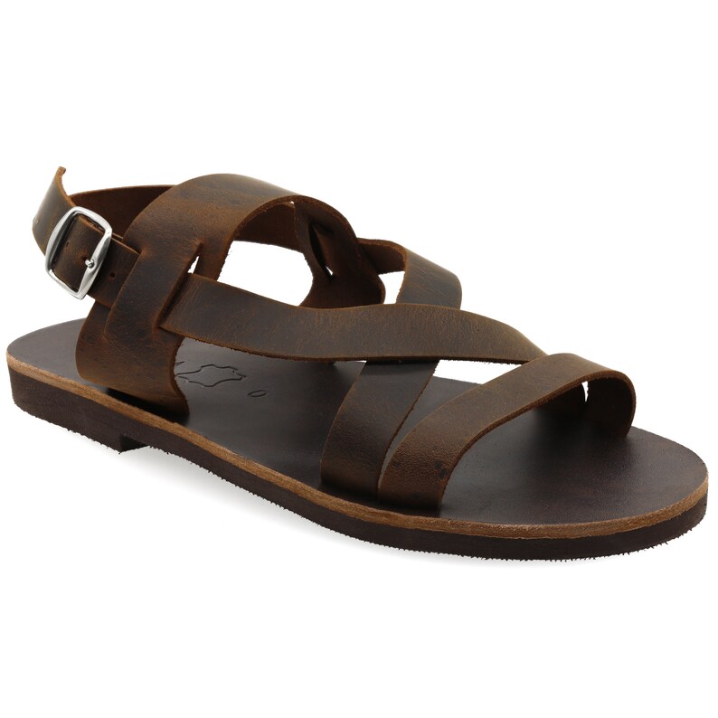 May include: Brown leather sandals with a criss-cross strap design and an adjustable ankle strap with a silver buckle.