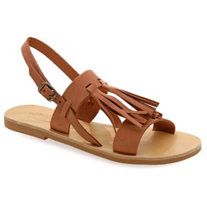 May include: Tan leather sandal with a flat sole and an ankle strap with a buckle. The sandal has a decorative fringe detail on the upper strap. The footwear is a neutral colour and appears to be made of high-quality leather.