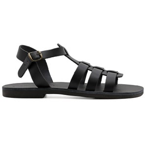 May include: Black leather sandals with a cage-like design. The sandals feature multiple straps across the foot and ankle, with a buckle closure. The sole is flat and the sandals have a classic, minimalist style.