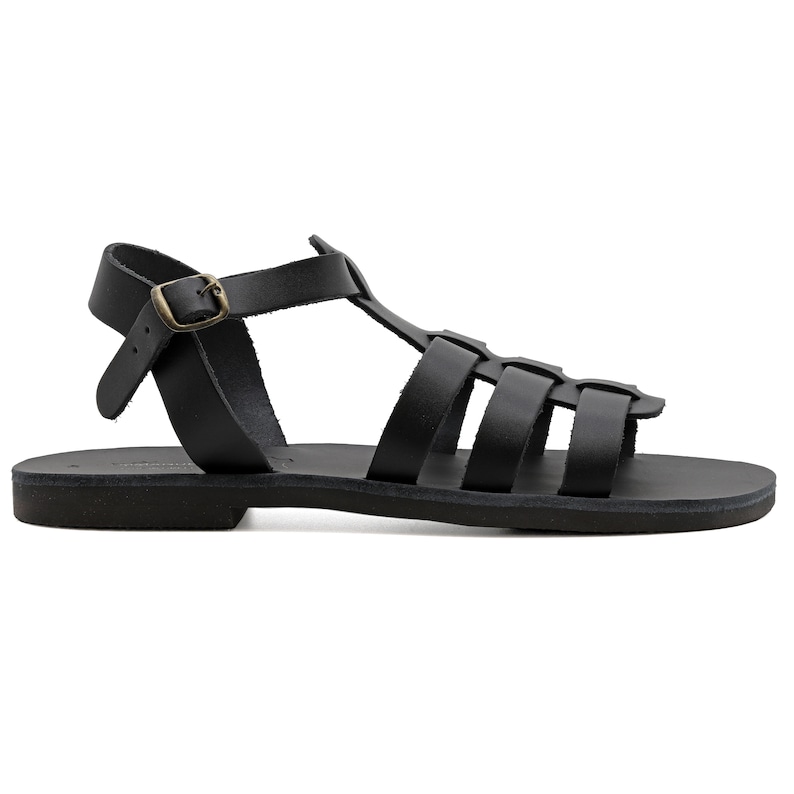 May include: Black leather sandals with a cage-like design. The sandals feature multiple straps across the foot and ankle, with a buckle closure. The sole is flat and the sandals have a classic, minimalist style.