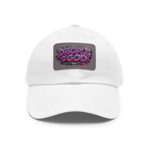 Può includere: Un cappellino da baseball bianco con una toppa rettangolare sul davanti. La toppa è grigia con una grafica in stile graffiti viola e rosa che recita "DISCIPLE OF GOD" con un testo più piccolo sotto che dice "IF YOU HOLD TO MY TEACHING, YOU ARE REALLY MY DISCIPLES. JOHN 8:31."
