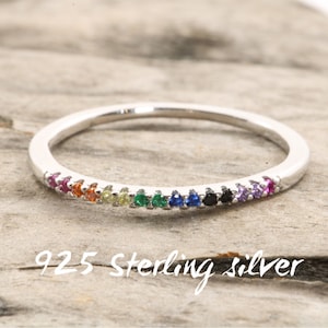 May include: A thin silver band ring with a rainbow of small gemstones set in the band. The text "925 Sterling Silver" is written below the ring.