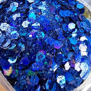 May include: A close-up view of a bag filled with iridescent blue glitter. The glitter is a mix of small and large hexagons and circles.