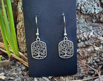 May include: A pair of silver earrings with a tree of life design. The earrings are on a black card.