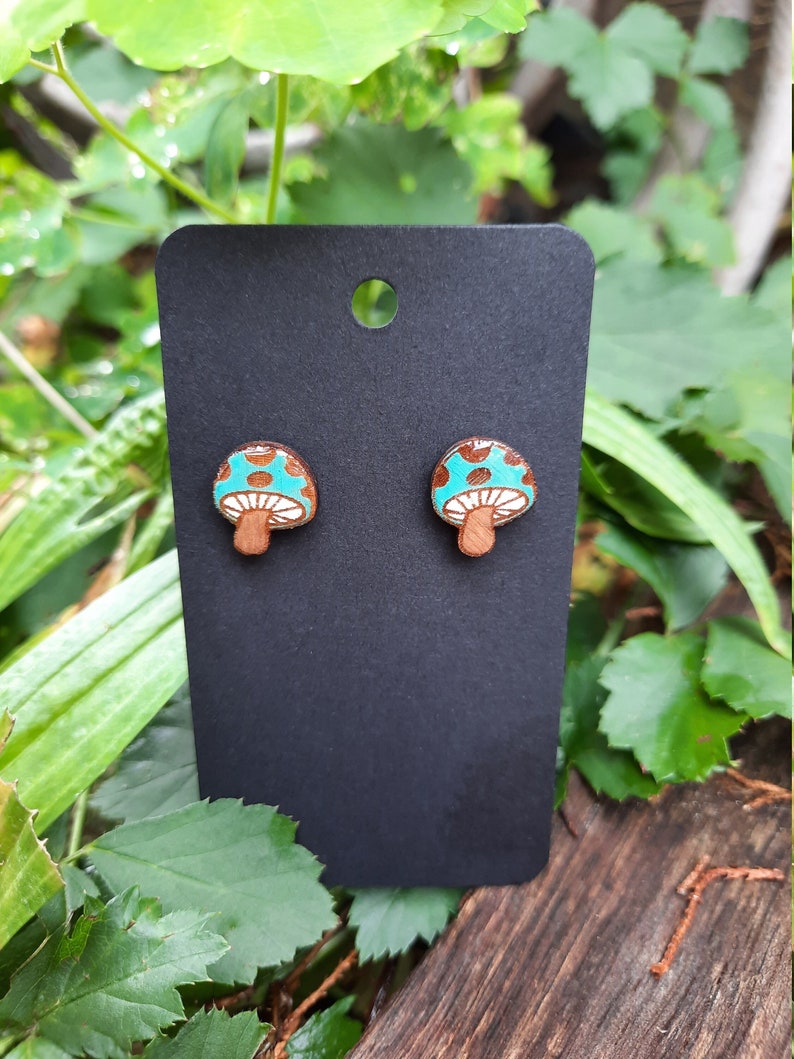 May include: A pair of mushroom-shaped earrings with a teal blue top, brown stem, and white polka dots.