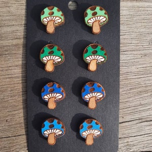 May include: Six pairs of wooden mushroom earrings. Three pairs are green with white polka dots and three pairs are blue with white polka dots.
