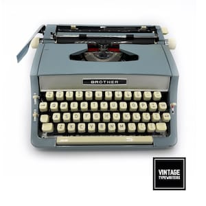 May include: A vintage Brother typewriter in a light blue color. The typewriter has a full keyboard with white keys and a silver carriage. The word "BROTHER" is displayed on the front. The image also includes a logo that says "VINTAGE TYPEWRITERS".