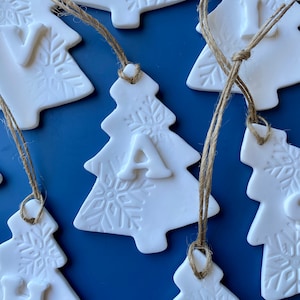 May include: White ceramic Christmas tree decorations with snowflake designs and letters spelling "JOY" hanging from twine.