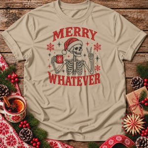 May include: A beige t-shirt featuring a graphic of a skeleton wearing a red Santa hat, holding a red mug, and making a peace sign. The text MERRY WHATEVER is printed in red above and below the skeleton, surrounded by red snowflakes.