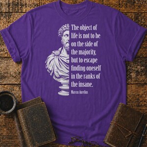 May include: A purple short-sleeved t-shirt featuring a white graphic of a Marcus Aurelius bust on the left side and the text: The object of life is not to be on the side of the majority, but to escape finding oneself in the ranks of the insane.