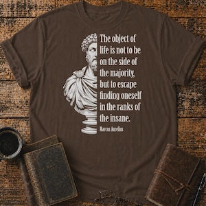 May include: A dark brown short-sleeved t-shirt featuring a white graphic of a Roman bust on the left and the text: The object of life is not to be on the side of the majority, but to escape finding oneself in the ranks of the insane. Marcus Aurelius.