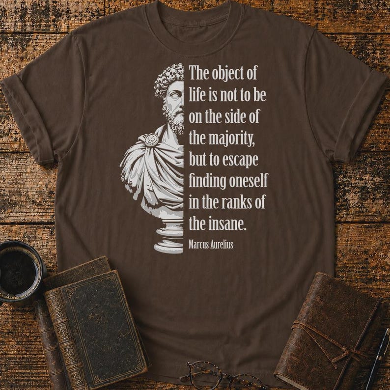 May include: A dark brown short-sleeved t-shirt featuring a white graphic of a Roman bust on the left and the text: The object of life is not to be on the side of the majority, but to escape finding oneself in the ranks of the insane. Marcus Aurelius.