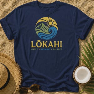 May include: A navy blue short-sleeved t-shirt featuring a circular graphic of a mountain, sun, and ocean waves. Below the graphic, the text reads LŌKAHI in large letters, followed by the words UNITY, HARMONY, and BALANCE in a smaller font.