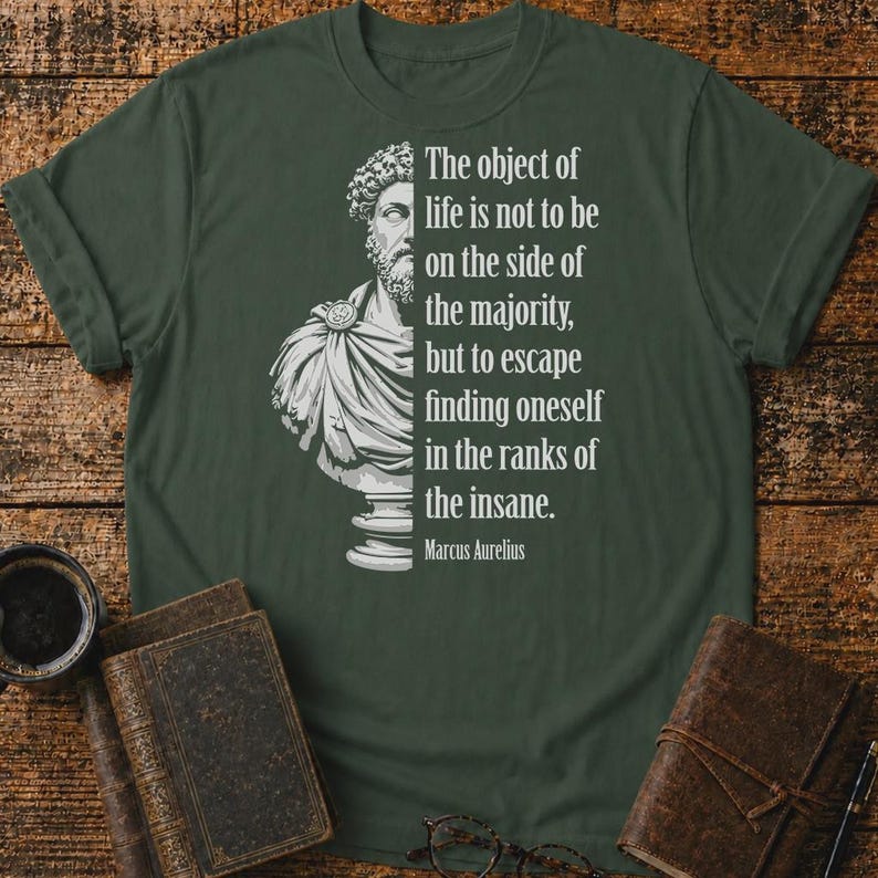May include: A dark olive green t-shirt featuring a white graphic of a Roman bust on the left side and the text: The object of life is not to be on the side of the majority, but to escape finding oneself in the ranks of the insane. Marcus Aurelius.