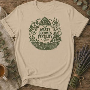 Może przedstawiać: Beżowy t-shirt z krótkim rękawem z okrągłym, ciemnozielonym nadrukiem graficznym. Wzór przedstawia cykl kompostowania z roślinami, grzybami i robakiem, otaczający tekst "WASTE BECOMES FERTILITY" wyśrodkowany pogrubioną czcionką.