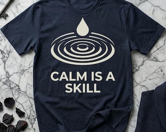 May include: Navy blue t-shirt with a white graphic of a water droplet and concentric circles. The text "CALM IS A SKILL" is printed below the graphic in white. The shirt is short-sleeved.
