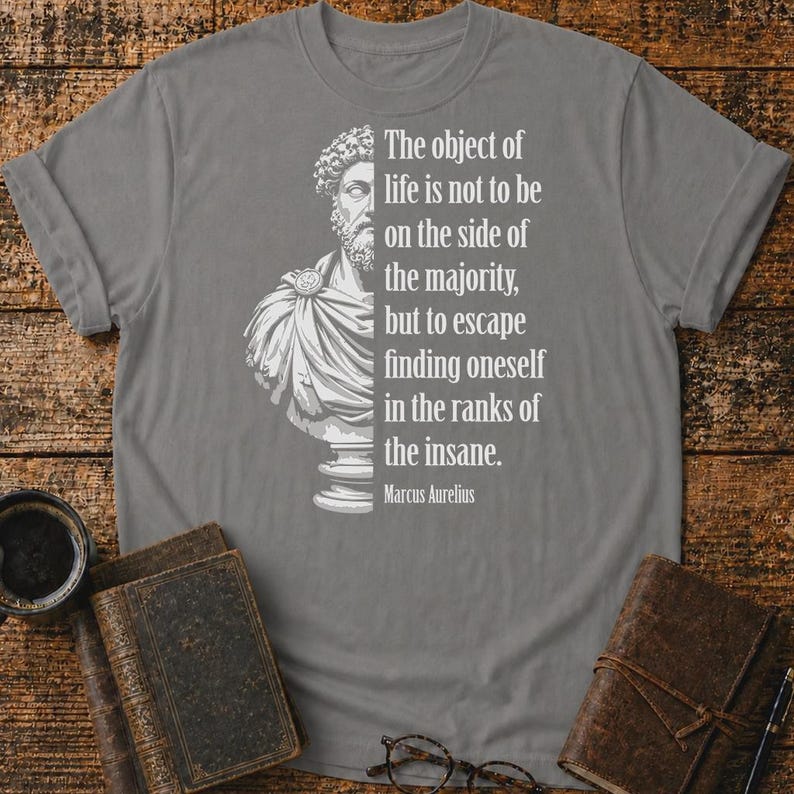 May include: A grey t-shirt featuring a white graphic of a Marcus Aurelius bust on the left and the text: The object of life is not to be on the side of the majority, but to escape finding oneself in the ranks of the insane. Marcus Aurelius.