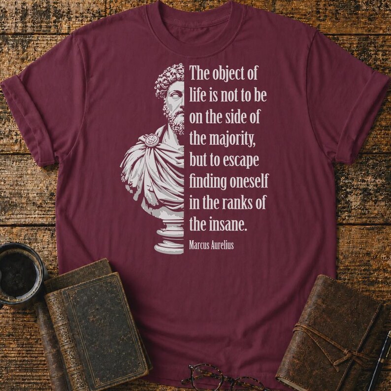 May include: A maroon short-sleeved t-shirt featuring a white graphic of a Roman bust and the text: The object of life is not to be on the side of the majority, but to escape finding oneself in the ranks of the insane. Marcus Aurelius.