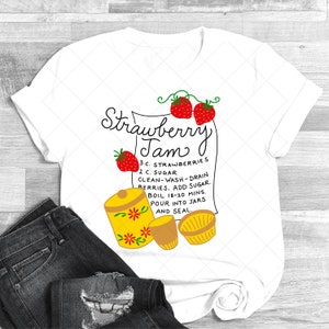 May include: White t-shirt with a red and green illustration of strawberries and a yellow jar with flowers. The text reads "Strawberry Jam" and includes a recipe for making strawberry jam.
