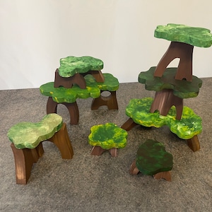 Puede incluir: Un conjunto de árboles de juguete de madera con follaje verde y troncos marrones. Los árboles están apilados uno encima del otro, creando una escena de bosque caprichosa.