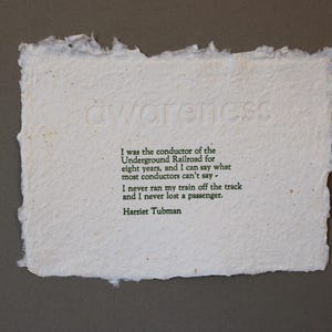 Pode incluir: Um pedaço de papel branco com uma citação de Harriet Tubman sobre seu trabalho na ferrovia subterrânea. A citação diz: "Eu era o condutor da ferrovia subterrânea por oito anos, e posso dizer o que a maioria dos condutores não pode dizer: nunca descarrilhei meu trem e nunca perdi um passageiro."