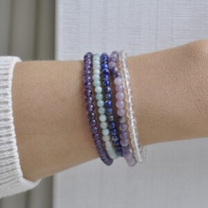 Puede incluir: Un conjunto de seis pulseras de cuentas en tonos morados, azules y blancos. Las pulseras est&aacute;n hechas de amatista, lapisl&aacute;zuli, aguamarina y cuarzo transparente.