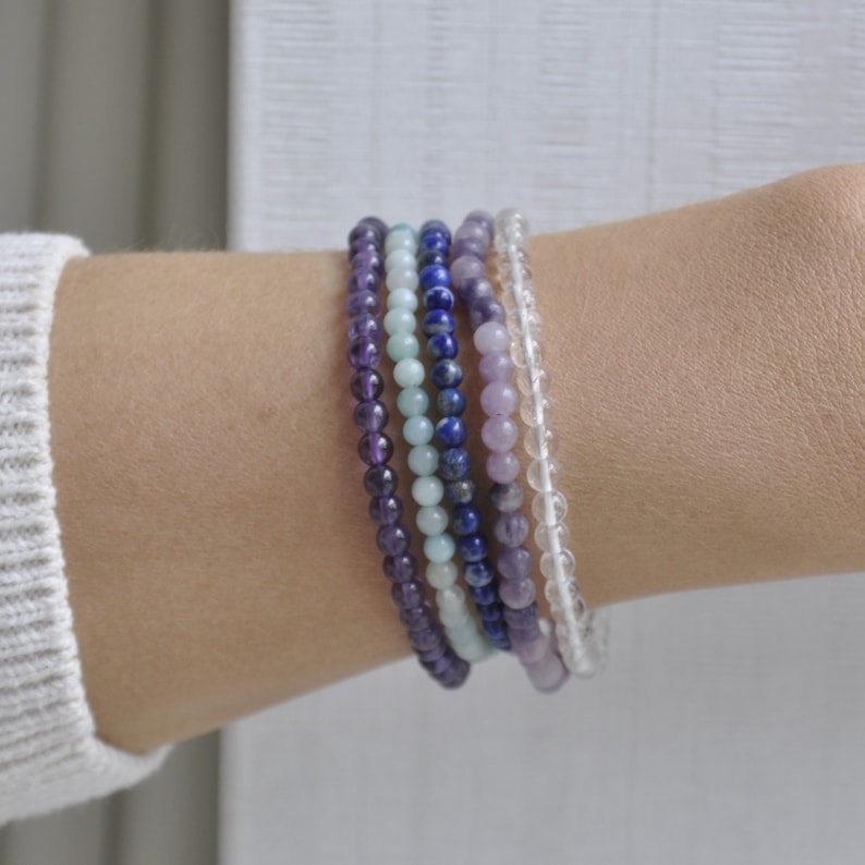 Puede incluir: Un conjunto de seis pulseras de cuentas en tonos morados, azules y blancos. Las pulseras est&aacute;n hechas de amatista, lapisl&aacute;zuli, aguamarina y cuarzo transparente.