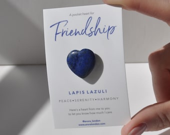 Op de afbeelding: Een kleine blauwe hartvormige lapis lazuli steen met de woorden "A pocket heart for Friendship" en "Lapis Lazuli Peace Serenity Harmony" op een witte kaart. De kaart bevat ook de tekst "Here's a heart from me to you to let you know how much I care" en het websiteadres "www.aroralondon.com".
