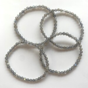 May include: Four grey beaded bracelets made of labradorite gemstones. The bracelets are stacked on top of each other.