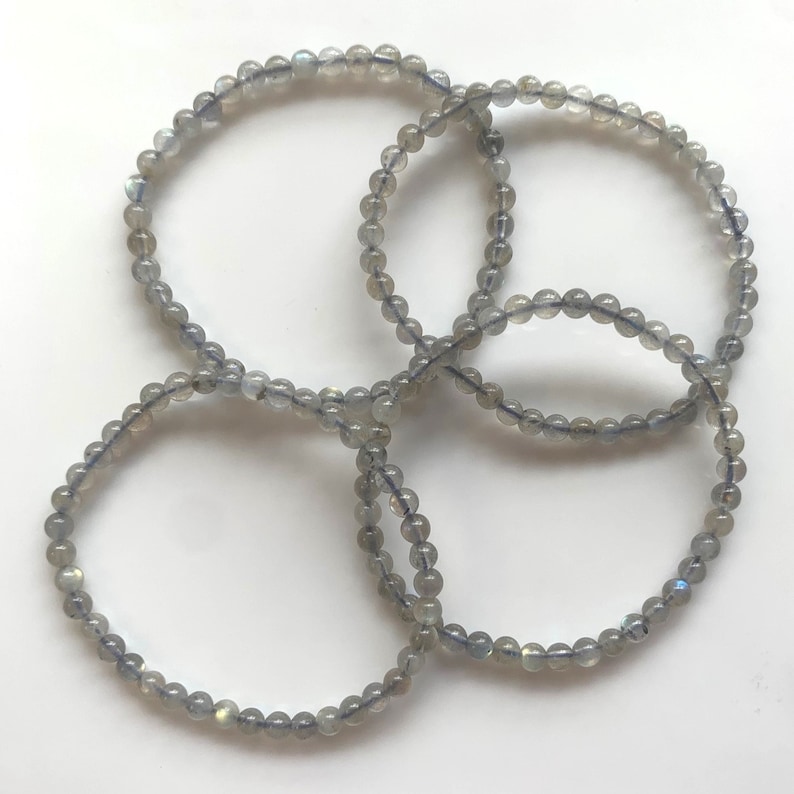 May include: Four grey beaded bracelets made of labradorite gemstones. The bracelets are stacked on top of each other.