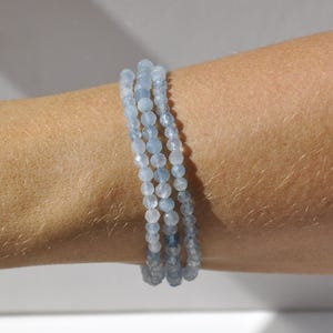 May include: A triple-strand bracelet made of light blue aquamarine beads. The beads are faceted and have a subtle shimmer.