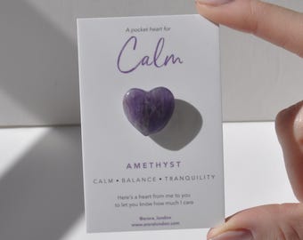 Op de afbeelding: Een klein paars amethist hartkristal op een witte kaart met de tekst "A pocket heart for Calm" en "AMETHYST CALM BALANCE TRANQUILITY" en "Here's a heart from me to you to let you know how much I care @arora_london www.aroralondon.com".