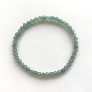 Pu&ograve; includere: Un delicato braccialetto composto da piccole perline rotonde verde chiaro. Le perline sono infilate insieme per formare un cerchio completo, appoggiato su una superficie bianca. Il braccialetto &egrave; un gioiello semplice ed elegante.