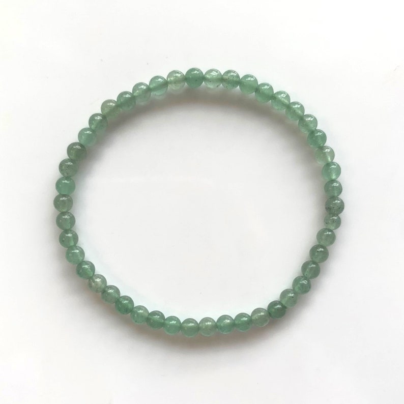 Pu&ograve; includere: Un delicato braccialetto composto da piccole perline rotonde verde chiaro. Le perline sono infilate insieme per formare un cerchio completo, appoggiato su una superficie bianca. Il braccialetto &egrave; un gioiello semplice ed elegante.