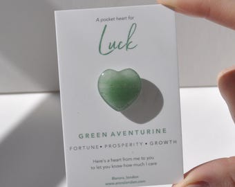 Op de afbeelding: Een hartvormig kristal van groene aventurijn op een witte kaart met de tekst "A pocket heart for Luck" en "GREEN AVENTURINE FORTUNE PROSPERITY GROWTH". De kaart bevat ook de tekst "Here's a heart from me to you to let you know how much I care" en "@arora_london www.aroralondon.com".
