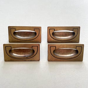 May include: Four antique brass drawer pulls. Each pull features a rectangular backplate and a curved handle. The pulls have a warm, aged patina, indicating vintage or reclaimed hardware. Suitable for furniture restoration or adding a vintage touch.