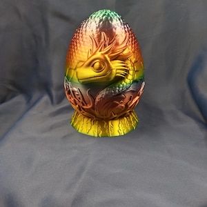 May include: A rainbow iridescent dragon egg with a detailed dragon head sculpted into the side. The egg is made of a smooth, textured material and has a gold base.