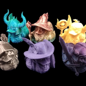 Könnte beinhalten: Eine Sammlung von sechs Fantasy-Figuren, jede mit einzigartigen Designs und Farben. Die Figuren umfassen einen türkisfarbenen Wikinger, einen bronzefarbenen Bogenschützen, einen kupferfarbenen Zauberer, einen gelben Engel, einen lila Zauberer und einen blau-violetten Ritter. Schwarzer Hintergrund.
