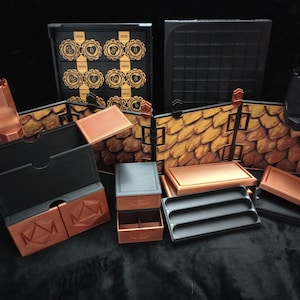 May include: A collection of tabletop gaming accessories, including modular walls with a scale-like texture, storage boxes, and trays. The pieces are primarily black and copper-colored, with some featuring decorative elements. The set appears to be designed for a fantasy or medieval-themed game.