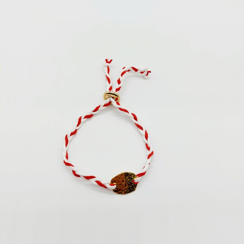 May include: A red and white braided bracelet with a gold oval charm.