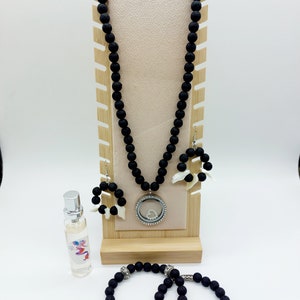 Puede incluir: Un conjunto de joyas de roca de lava negra, que incluye un collar con un dije de plata, aretes y dos pulseras. El collar y los aretes tienen detalles de conchas blancas.
